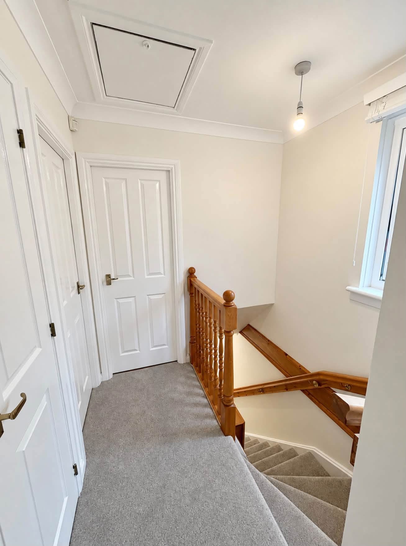 Hall, stairs and landing decorated by DJM Decor with light walls, white doors and trim, and a wooden stair banister